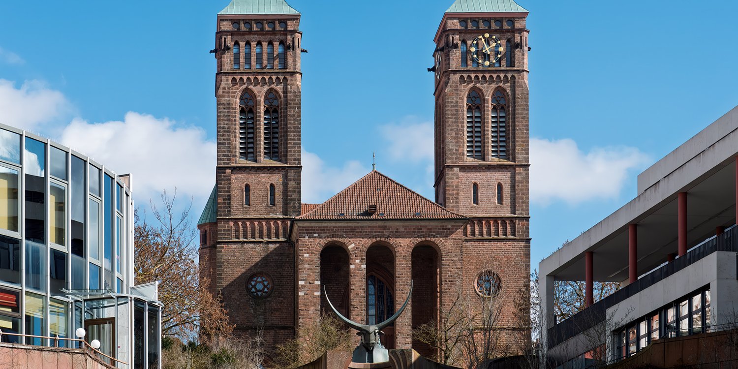Auf dem Schlossplatz in Pirmasens steht ein bronzener Stierkopf, im Hintergrund die Pirminiuskirche und eine breite Sandsteintreppe. Die Szene steht sinnbildlich für die Stadt, in der sich nun auch ein neuer Standort der BüchnerBarella Unternehmensgruppe befindet.