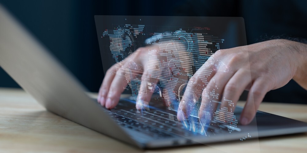 Eine Person tippt auf einem Laptop, dessen Bildschirm eine Weltkarte anzeigt. Das Konzept der Globalisierung und der weltweiten Vernetzung durch Technologie. Die Szene wirkt eher ernst und konzentriert.